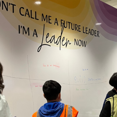 Three students in JA BizTown under a sign that reads, "I'm a Leader Now"