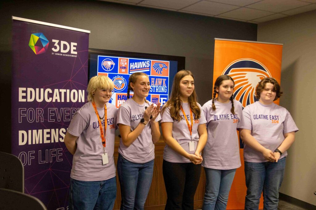A group of high school students presenting in front of a monitor and banners