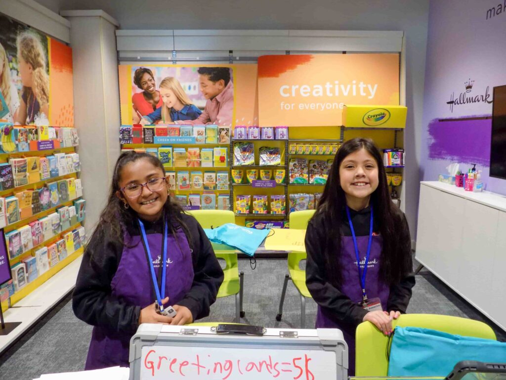 Two students smiling in front of a storefront with greeting cards at JA BizTown