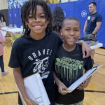 Two young students at a career fair holding clipboards and smiling
