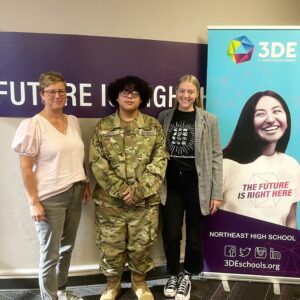 A student and two teachers standing in front of a 3DE banner, smiling