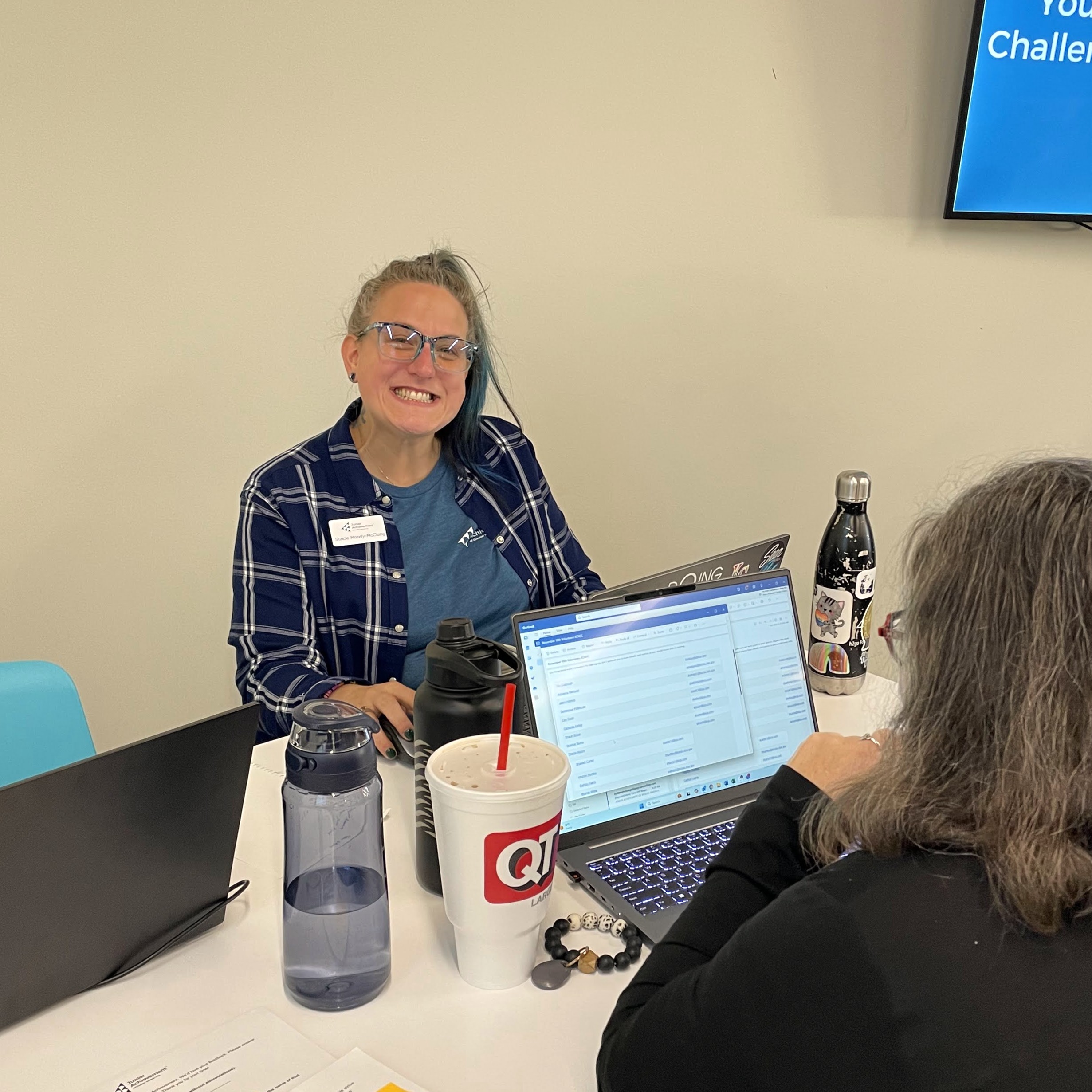 A woman sitting at a table working on a laptop, smiling at the camera