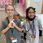 Two young students at JA BizTown holding a stuffed dog in front of a table with raffle prizes
