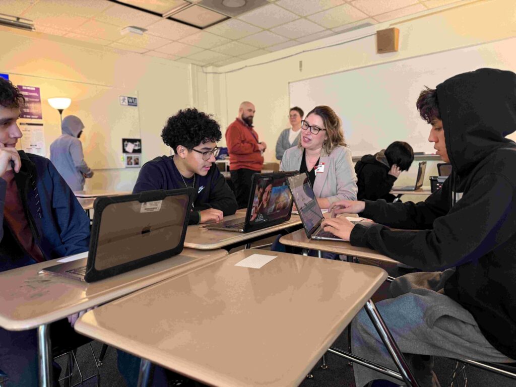 Three high school students working on laptops with a volunteer