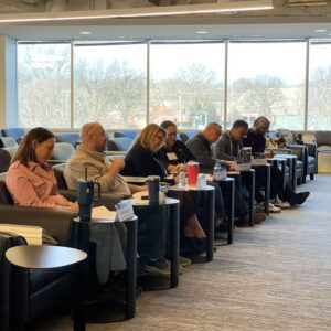 Group of people sitting in an auditorium, looking at the front of the room and writing notes on paper.