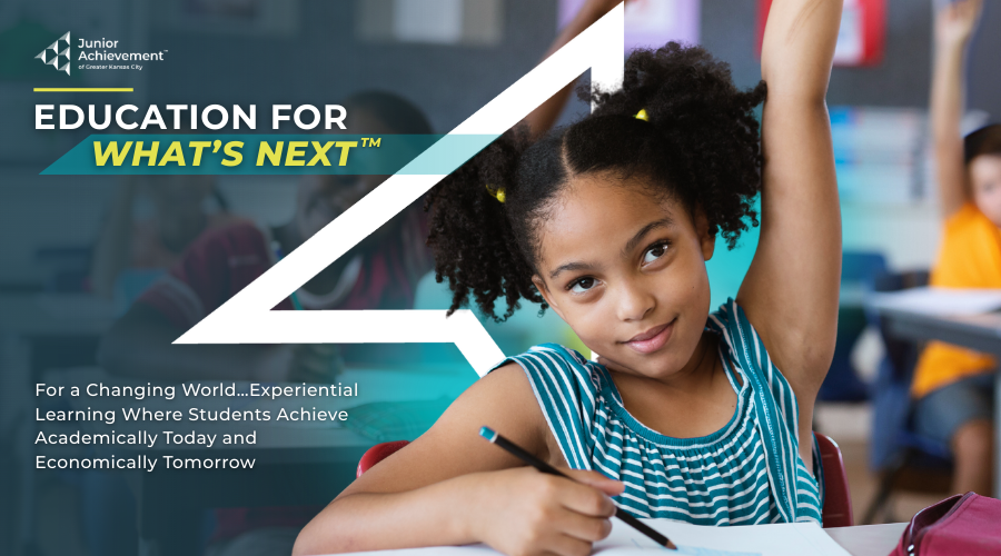 Young girl raising her hand and smiling in a classroom.