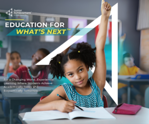 Young girl raising her hand and smiling in a classroom.