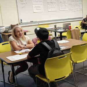 A volunteer sitting at a table in a classroom with a student.