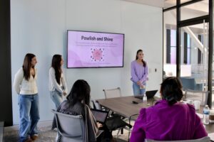 Three students standing by a screen at the front of a conference room giving a presentation.
