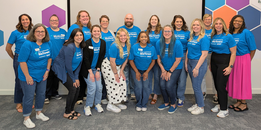 17 Junior Achievement staff members posing for group photo wearing Junior Achievement BizTown blue shirts