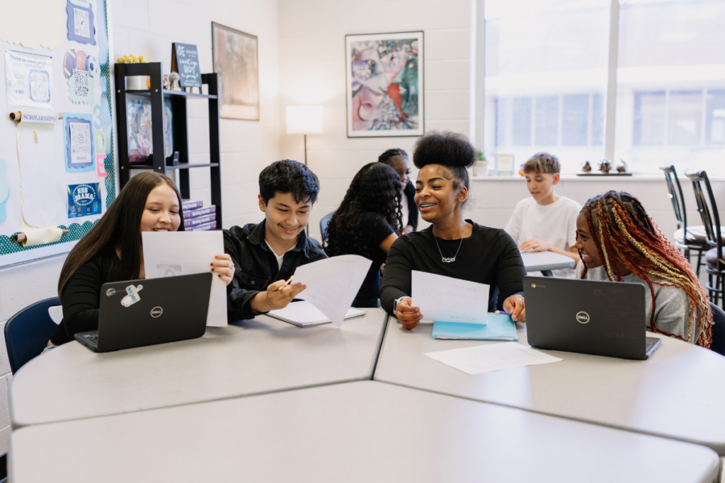 Group of students sitting at a table, looking at a piece of paper and laughing
