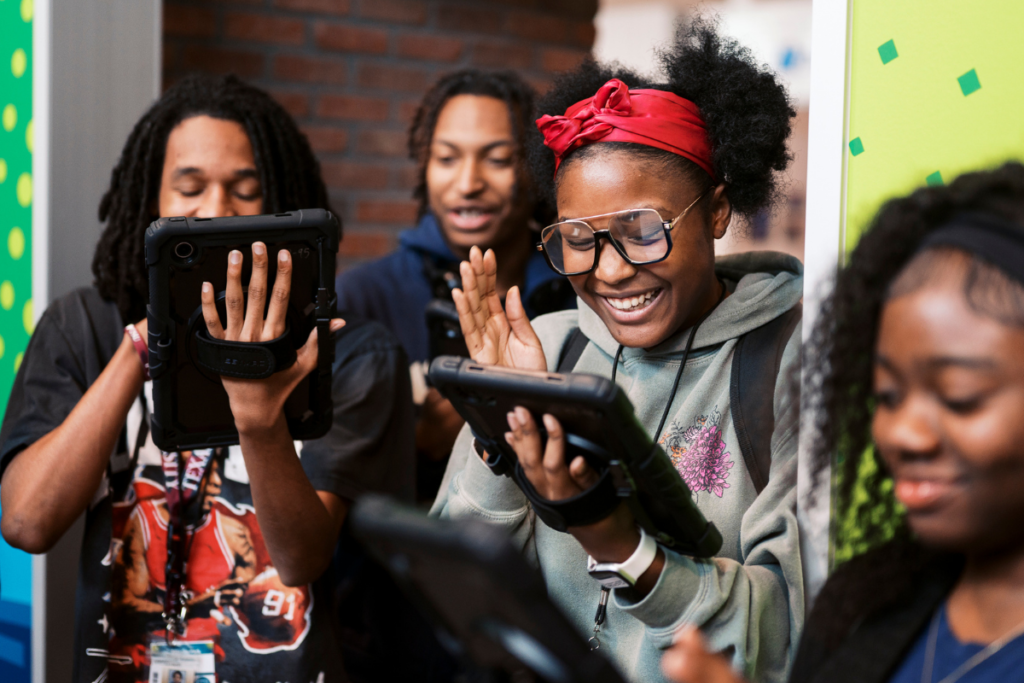 Group of students standing together and smiling, while looking at a tablet.