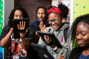 Group of students standing together and smiling, while looking at a tablet.